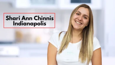 Shari Ann Chinnis from Indianapolis, smiling warmly with straight, light brown hair. She is wearing a white t-shirt and standing in a modern indoor space with a blurred background, possibly a kitchen. The atmosphere is casual and welcoming, with text overlaying the image that reads "Shari Ann Chinnis Indianapolis" in bold black font framed by a red border