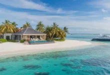 Make1m.com Luxury Vacations overwater bungalows with thatched roofs on a secluded Maldivian island, available for booking on make1m.com. Palm trees surround the bungalows, and a private beach with clear turquoise water beckons