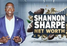 This image features Shannon Sharpe, a former NFL player and well-known sports analyst, wearing a purple suit and glasses, smiling confidently. He is making a double peace sign gesture with both hands. Next to him is a bold graphic with the text "Shannon Sharpe Net Worth" in large white and gold letters. Surrounding the text are various symbols, including footballs, gold coins, a microphone, and an upward arrow on a bar chart, all symbolizing his financial success, media influence, and career in sports. The background is sleek and modern, with a professional aesthetic.