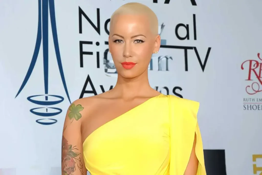 Amber Rose attending an award event in a yellow one-shoulder gown, showcasing her signature buzzcut and tattoos. Amber Rose net worth has grown significantly due to her modeling, acting, and business ventures.