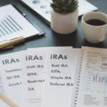 An organized desk featuring financial documents, a retirement planning notebook, a calculator, and tax forms, representing different types of IRAs such as Traditional, Roth, SEP, SIMPLE, and Rollover IRAs. A graph showing financial growth and a cup of coffee highlight strategic retirement planning.